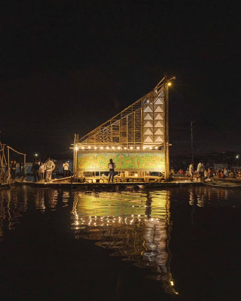 Floating platform with angled bamboo frame and glowing screen reflected in calm water at night