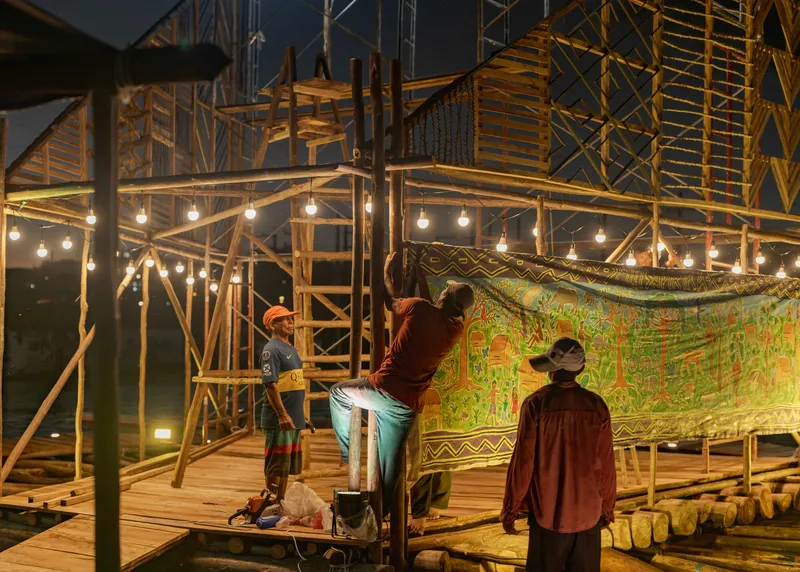 Timber scaffold structure with hanging bulb lights and a painted textile backdrop at dusk