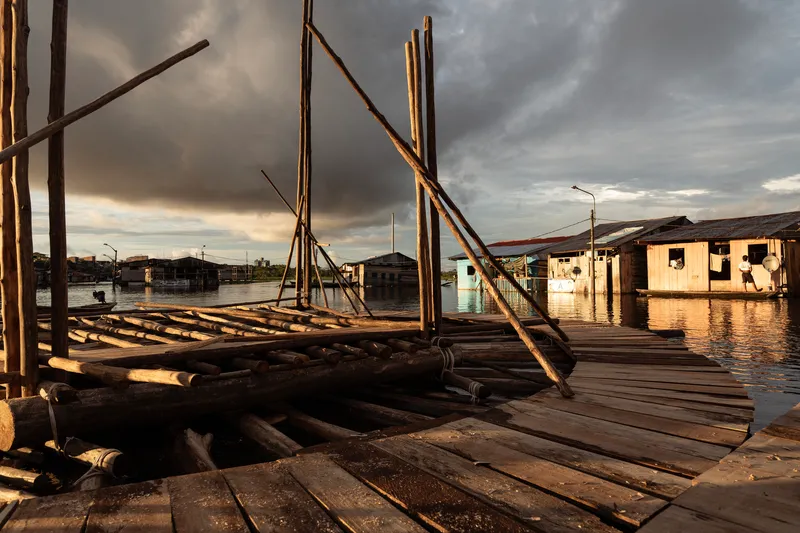 Floating timber deck platform with angled poles at golden hour beside waterside houses