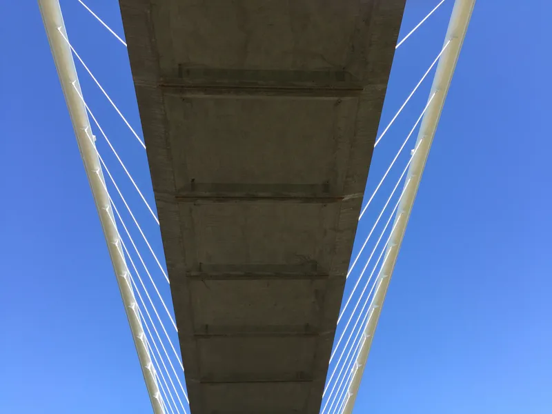 View from below showing the concrete deck underside framed by paired white arches and cable rigging