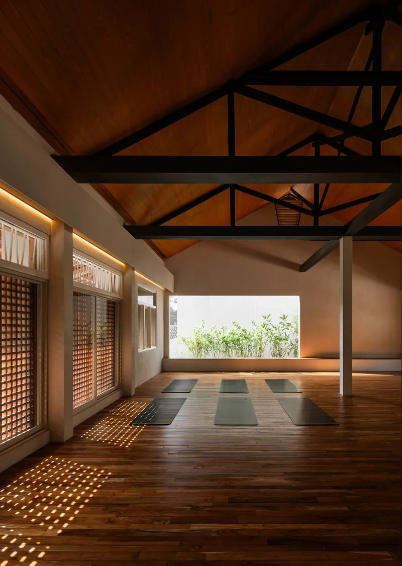 Wood-floored room with exposed steel truss ceiling and lattice screen windows filtering daylight
