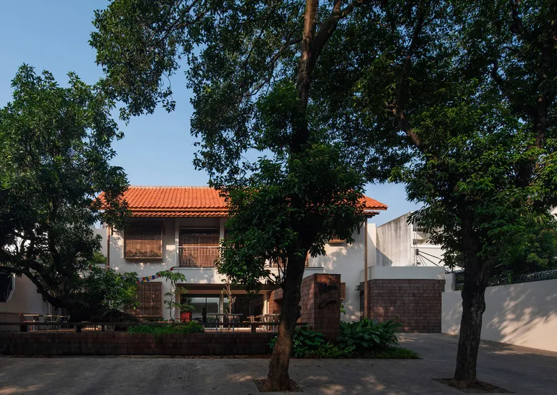 Street view showing white stucco volumes with red clay tile roofs framed by mature trees