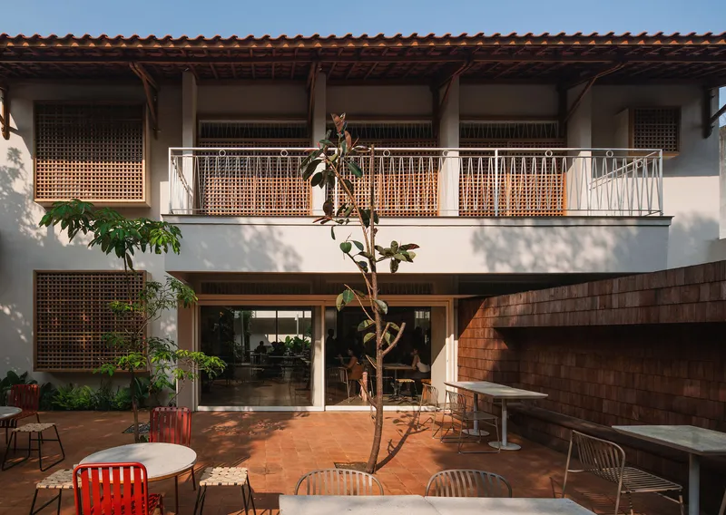 Interior courtyard with terracotta paving, lattice screens and a white metal balcony rail under afternoon sun