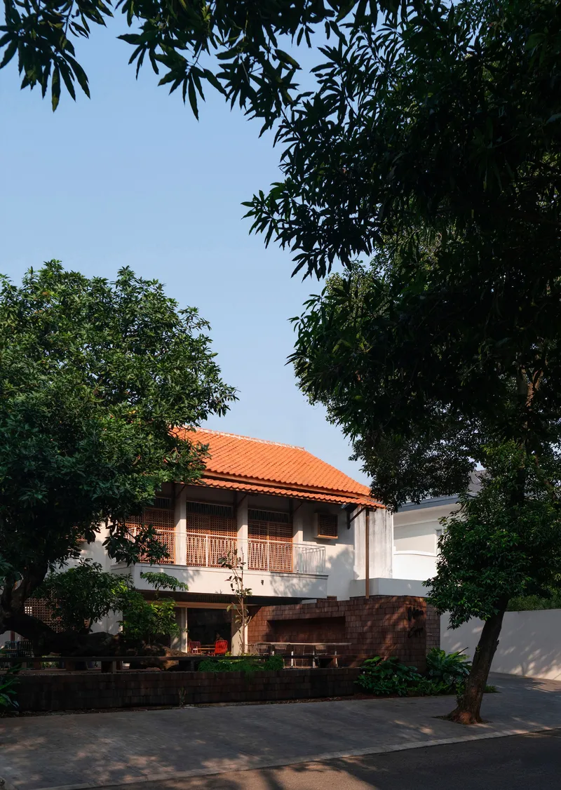 Two-storey facade with orange clay tile roof framed by overhanging tree canopy at dusk