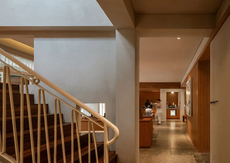 Curved timber staircase with vertical slat balustrade beside a terrazzo floor corridor with wood paneling