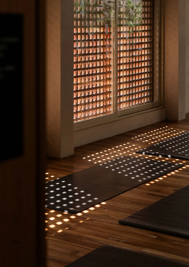 Perforated brick screen window casting dappled sunlight patterns across herringbone timber flooring