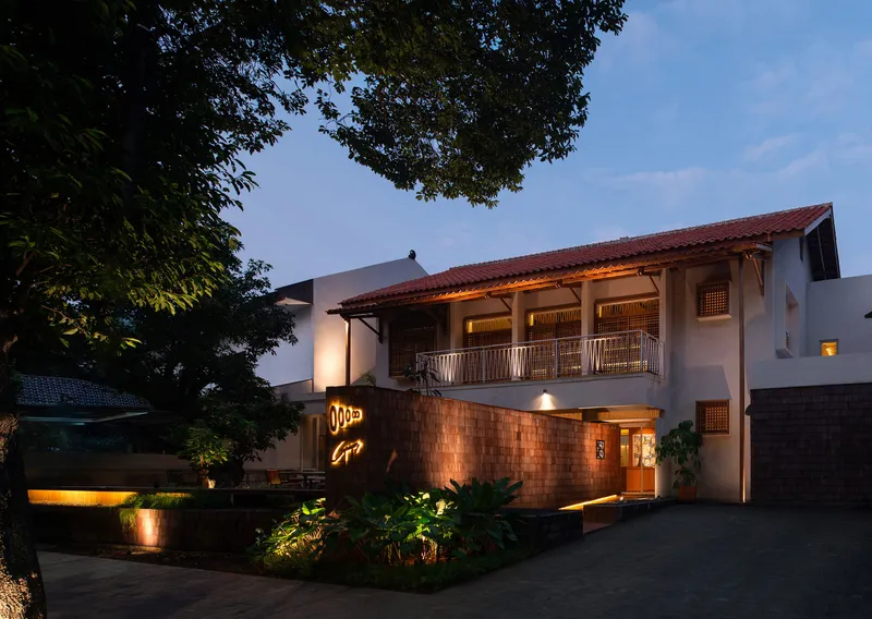 Two-story white stucco facade with timber balcony and red tile roof at dusk with landscape lighting