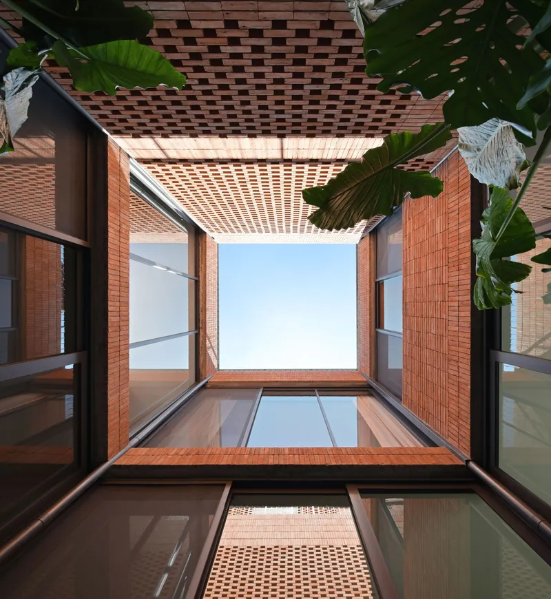 Upward view through perforated brick ceiling and glazed courtyard opening framed by banana leaves