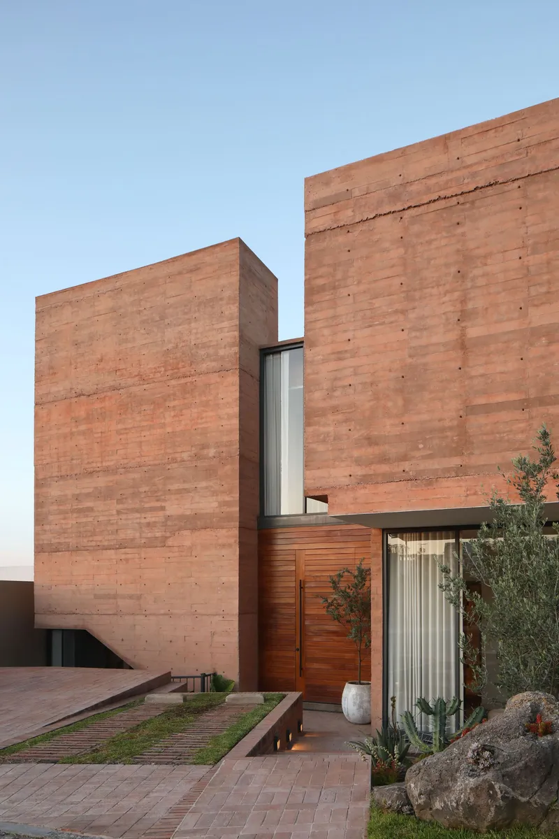 Entry courtyard framed by rammed earth walls and timber-clad volume with planted beds