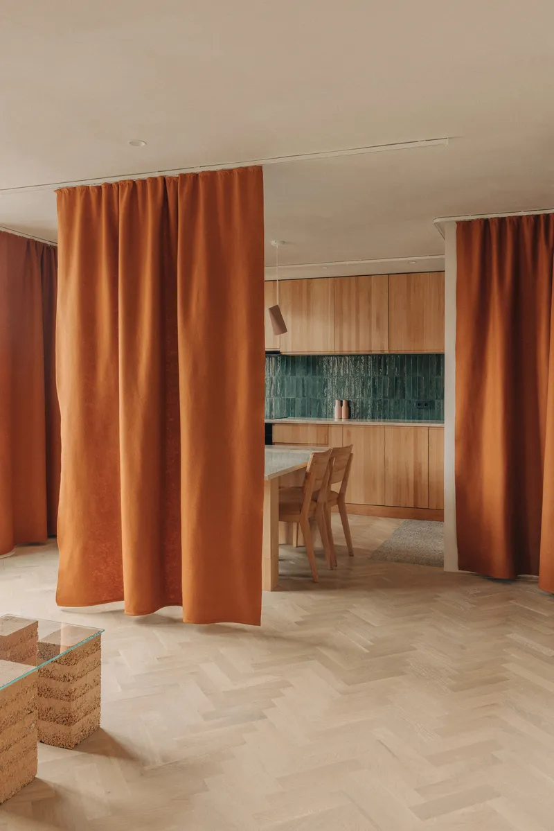 Floor-to-ceiling orange curtains dividing the living space from the kitchen with green tiled backsplash
