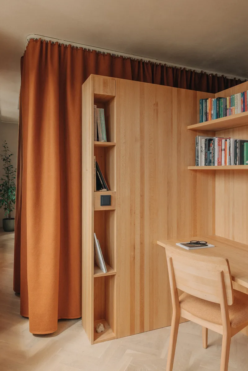 Timber bookshelf and desk with narrow vertical storage niche alongside an orange curtain