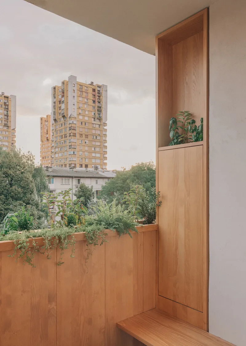 Timber balcony with planted boxes overlooking residential tower blocks under cloudy sky