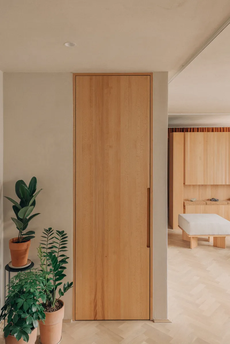 Timber door between white walls with potted plants and view into bathroom with freestanding tub