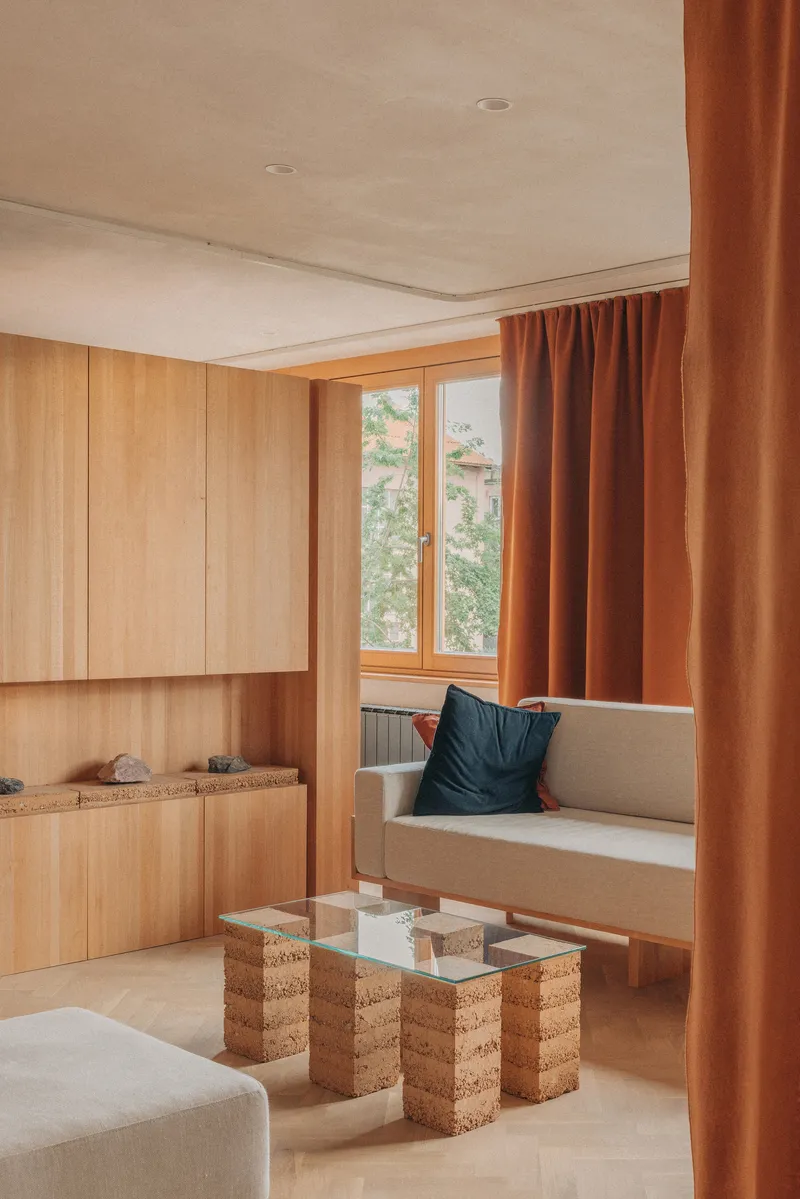 View through rust-colored curtains toward a timber-framed window with green foliage outside