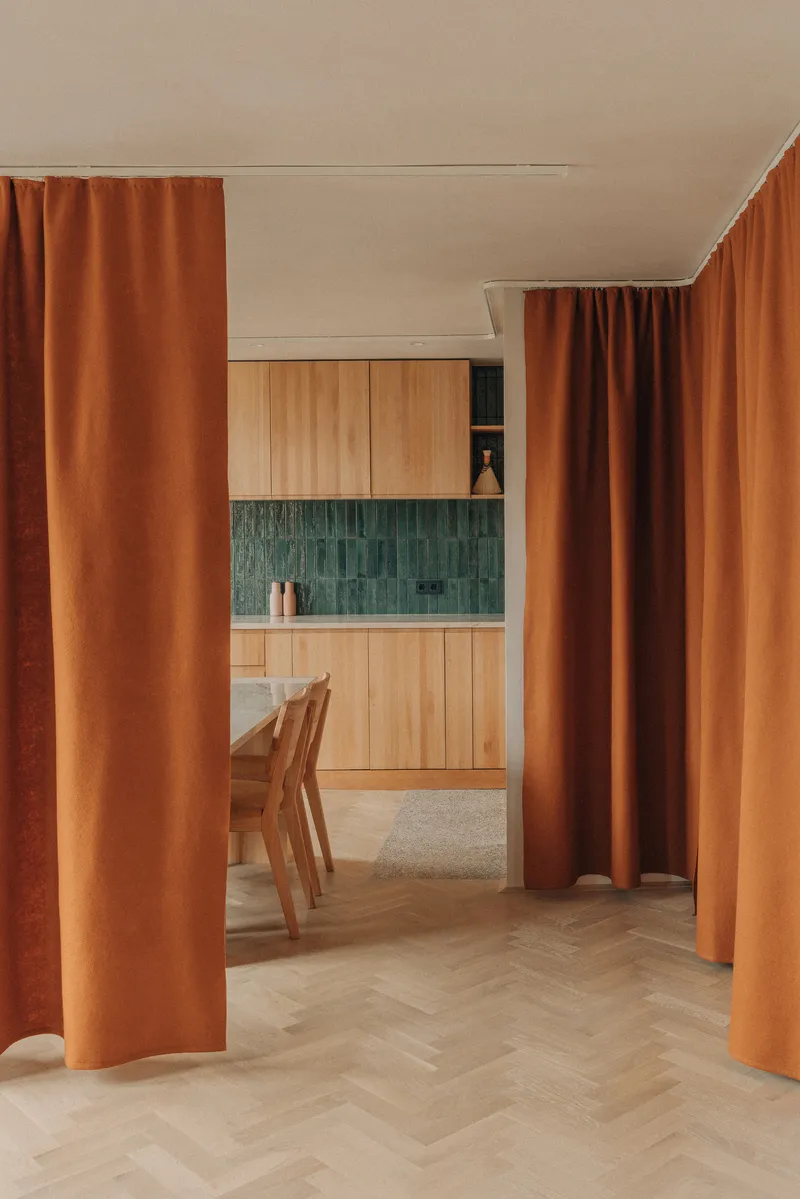 Herringbone oak flooring leading through terracotta drapes to a kitchen with green zellige tile backsplash