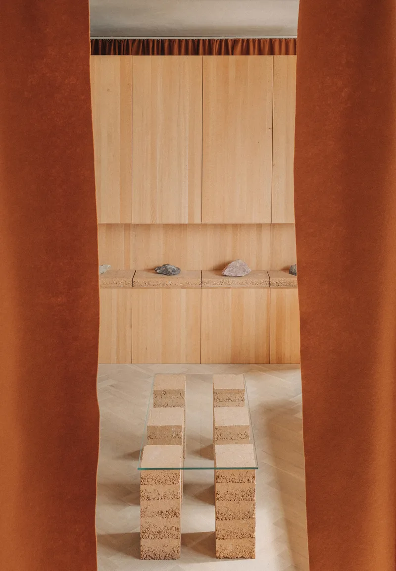 View through terracotta portal framing a light wood built-in bench with cork stools in front