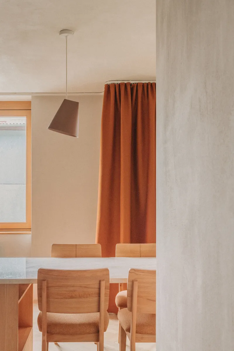 Dining area with timber chairs and pendant light framed by concrete column and terracotta curtain