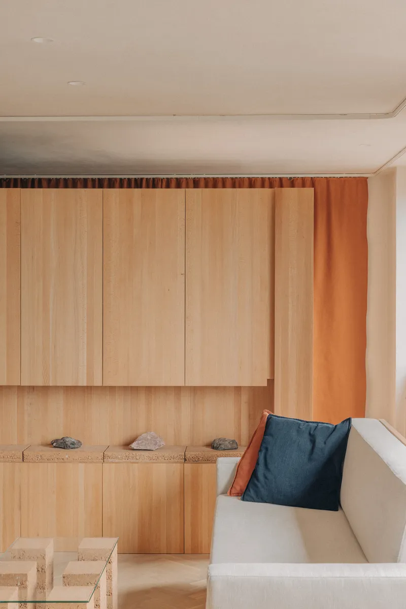 Built-in bench with blue cushion beside vertical timber cabinetry and an orange curtain