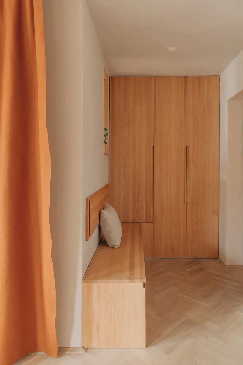 Entryway with timber wardrobe, integrated bench and herringbone flooring partially screened by orange curtain