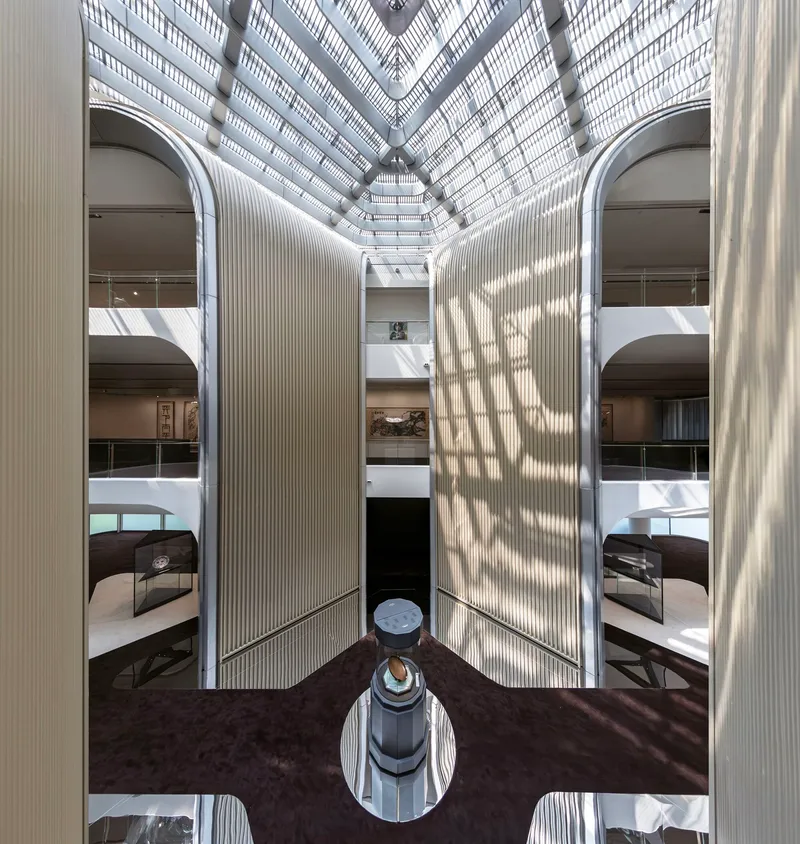 Looking up through a central atrium with ribbed column walls and geometric skylight above