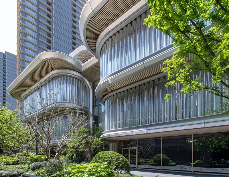 Layered curved balconies with vertical louvers and ribbed soffits framed by trees in sunlight