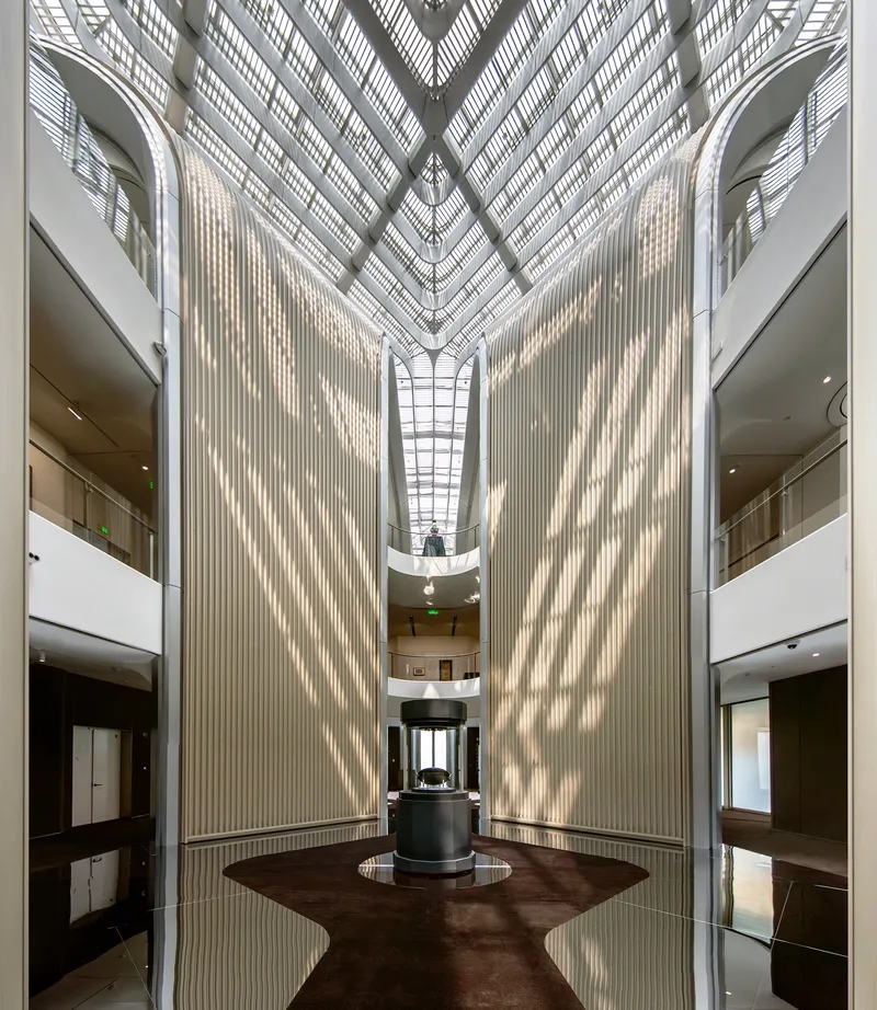 View up through atrium showing vertical ribbed walls and geometric glazed roof with natural light filtering down