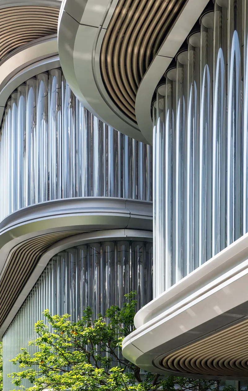 Curved balconies with vertical metal slats and ribbed soffits wrapping around planted greenery