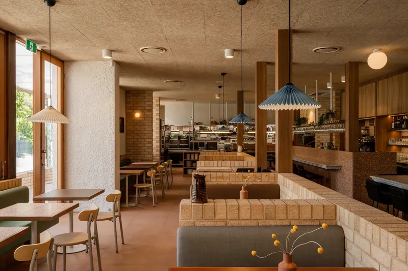 Open dining room showing cream tile partitions, pendant lights, and timber joinery under a textured concrete soffit