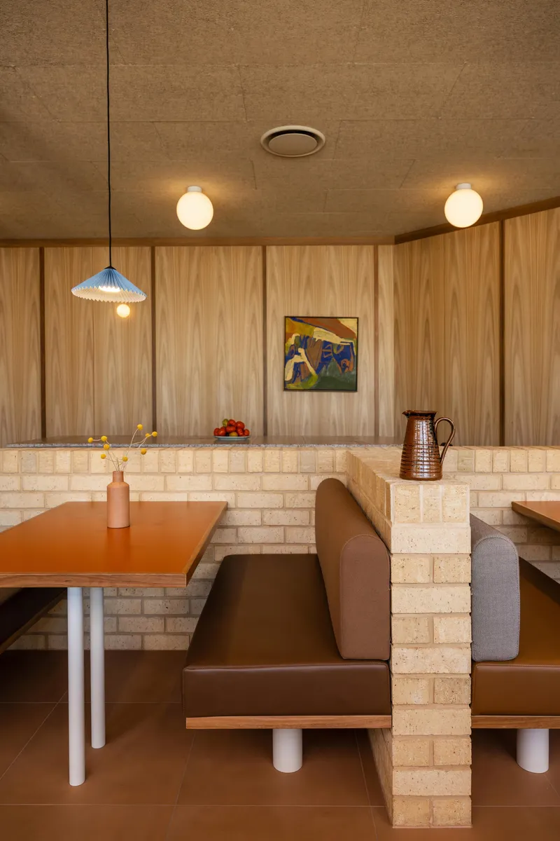 Corner booth with cream tile divider walls, orange laminate table, and globe pendant lights warming the space