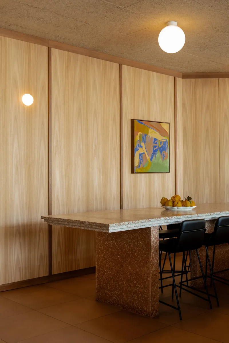 Terrazzo-clad counter island against a vertical timber-panelled wall with framed artwork and globe pendants