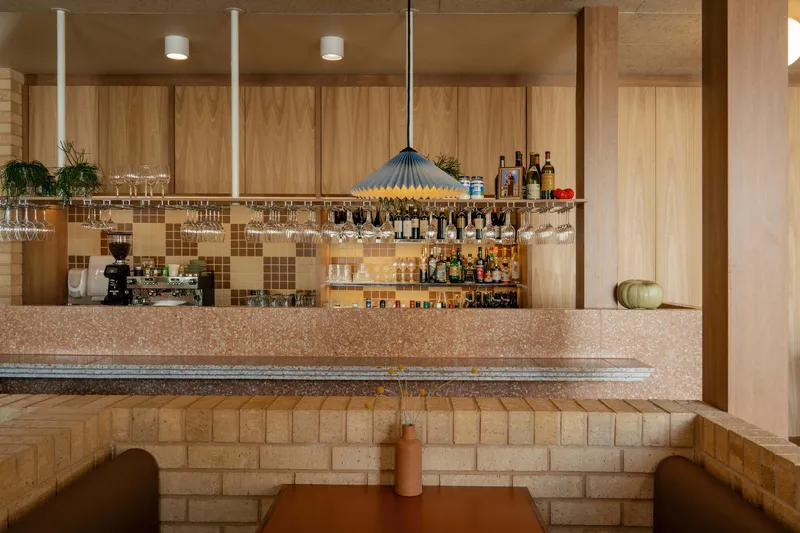 Bar counter with overhead glassware rack and mosaic tile backsplash beneath a fluted pendant light