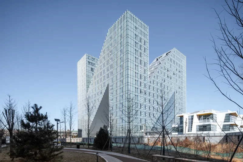 Three interconnected glass towers with vertical white fins rising above bare winter trees