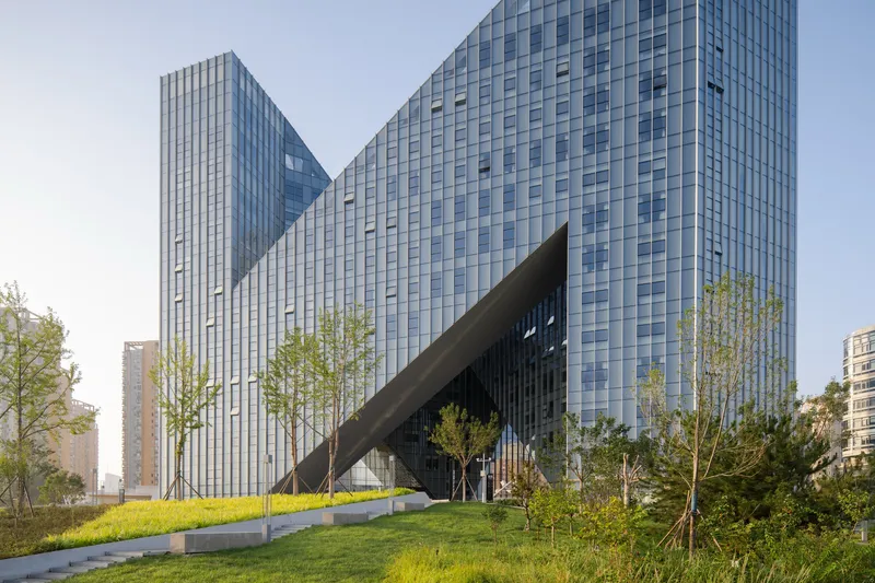 Ground-level view of the glass curtain wall facade with angled canopy over landscaped lawn