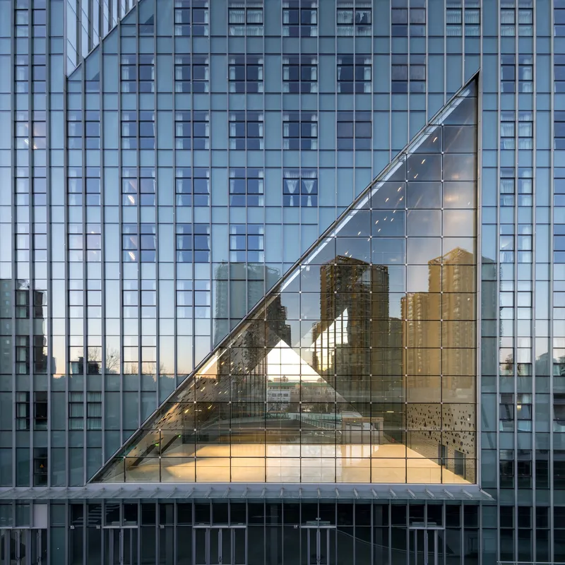 Triangular glass void in the tower facade reflecting neighboring buildings at dusk