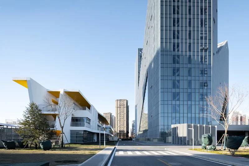 Glass tower and low building with yellow canopy elements along a concrete pathway