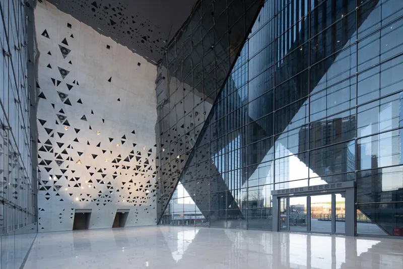 Glazed lobby with perforated concrete walls and triangular apertures in afternoon light
