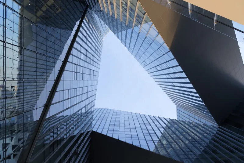 Upward view into triangular courtyard formed by glass curtain wall and angled metal panel facade