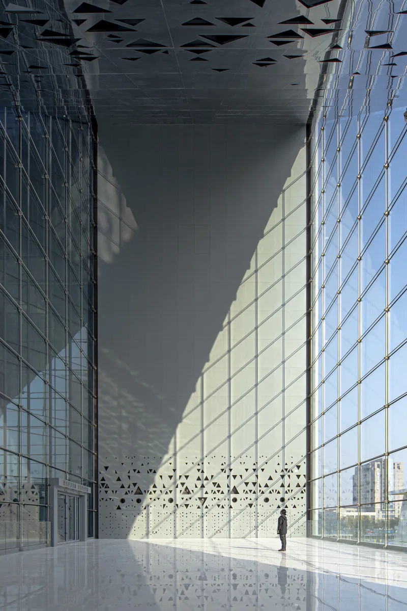 Lobby interior with perforated white wall, reflective floor, and glass curtain wall under patterned ceiling