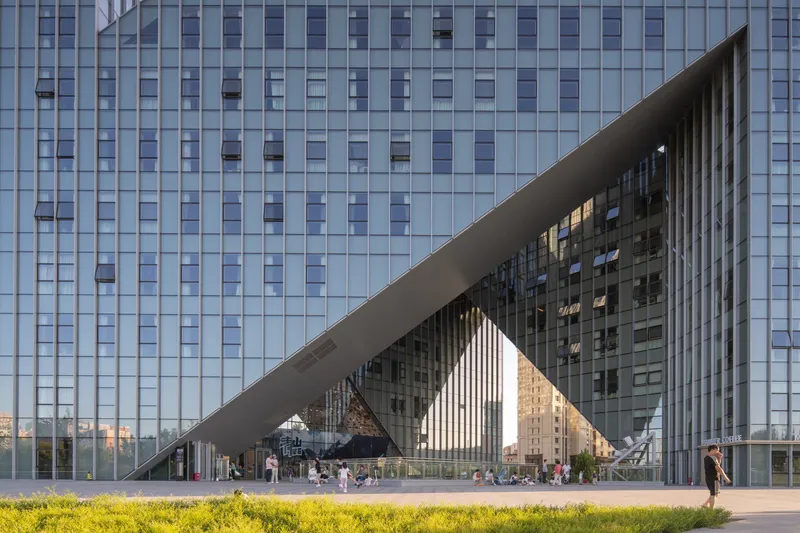 Ground level view of the sloped glass facade with diagonal canopy framing the entrance plaza