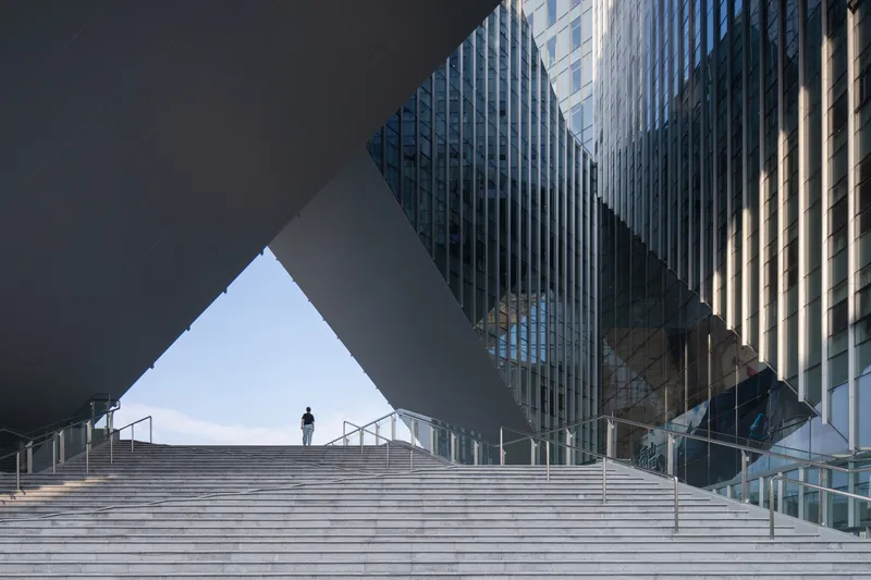Wide stone staircase ascending toward the triangular void carved beneath the angled overhang