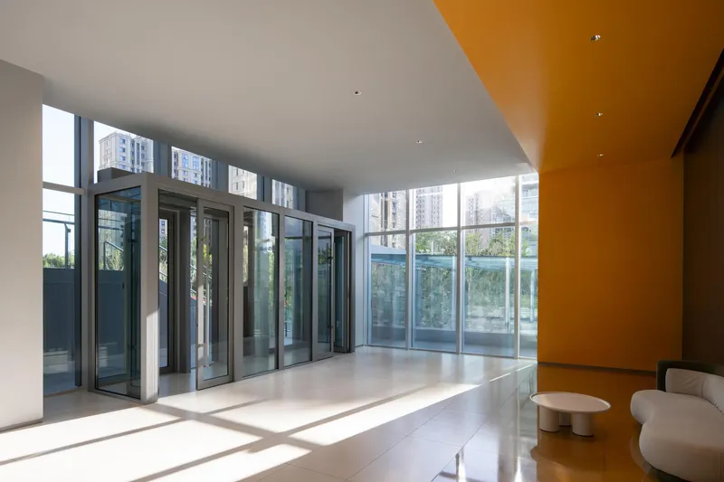 Interior lobby with floor-to-ceiling glazing, polished stone floors, and an angled orange ceiling panel