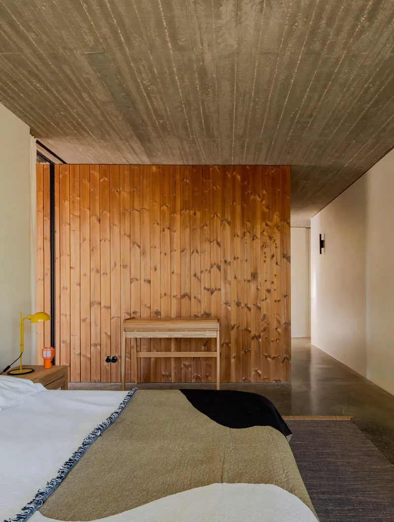 Bedroom interior with vertical timber wall panel enclosing sauna and board-formed concrete ceiling