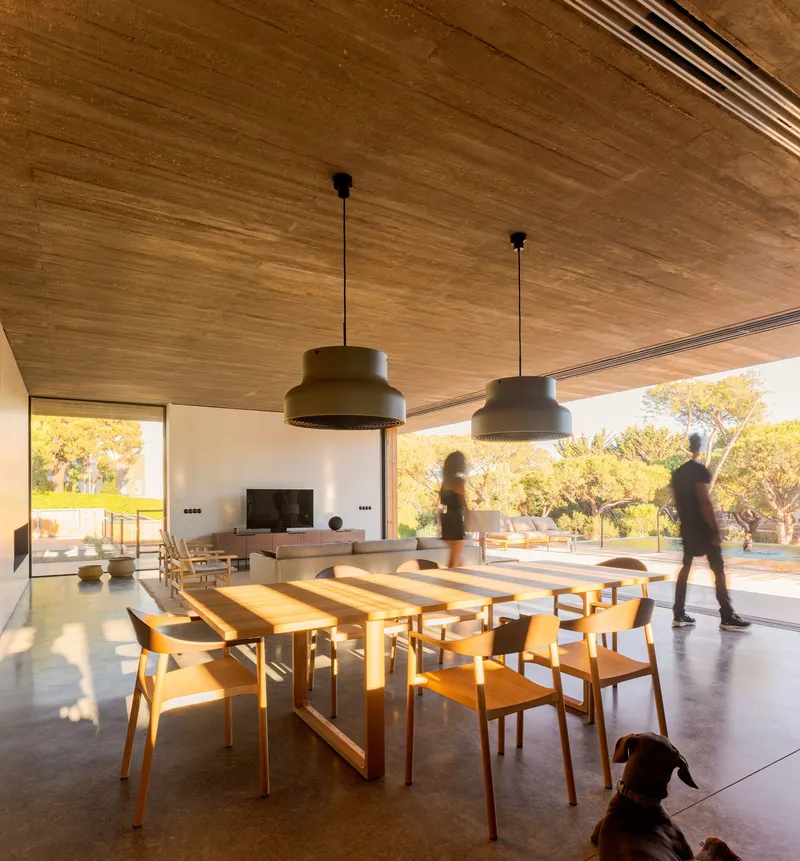 Dining area with timber table and pendant lights beneath a boarded ceiling as figures move through the space