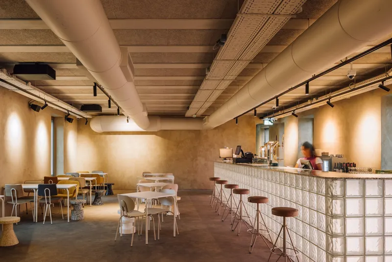 Cafe interior with glass block counter, exposed timber beams, ductwork, and scattered seating under track lighting