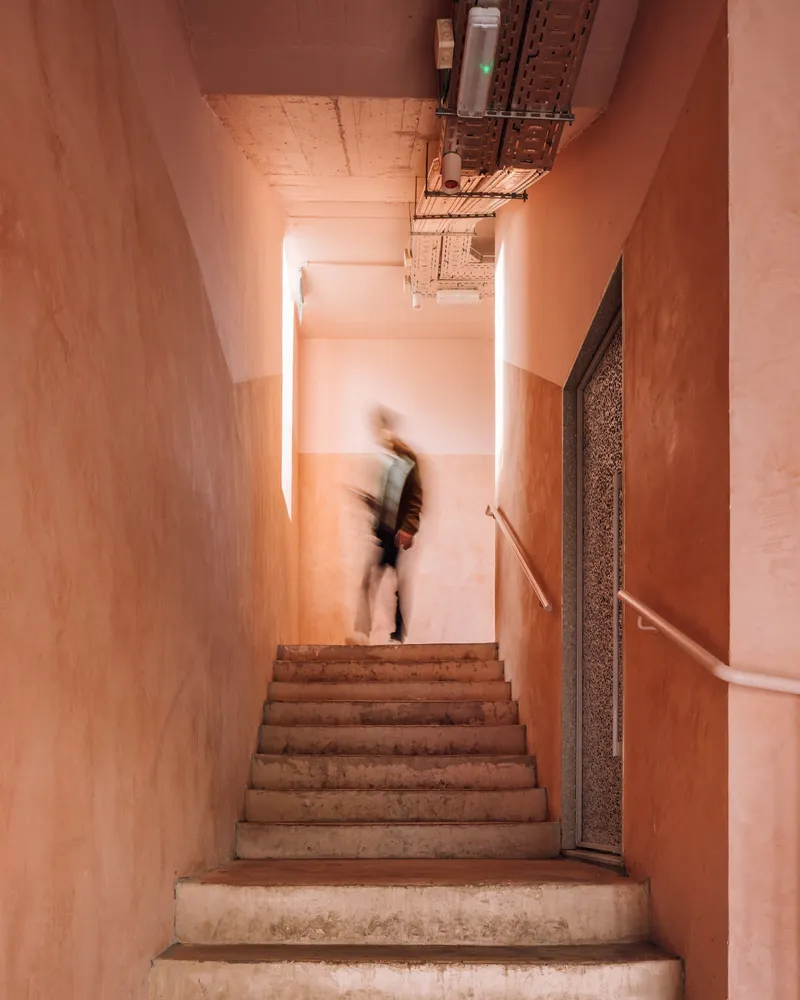 Narrow concrete staircase with pink plaster walls and a person in motion descending
