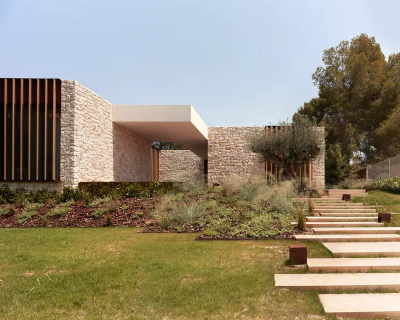 Terraced lawn with stone steps ascending toward covered entry portal framed by masonry and vertical metal fins