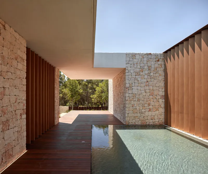 Covered passage with timber decking alongside reflecting pool flanked by stone walls and vertical metal screens