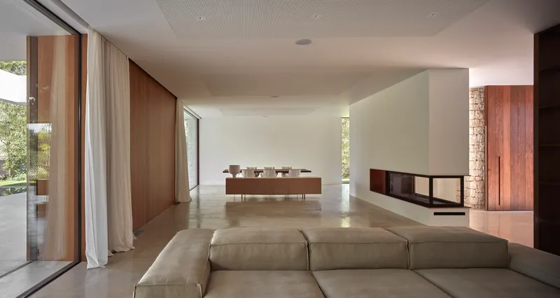 Open-plan living space with sectional sofa, dining island, and floor-to-ceiling windows overlooking garden