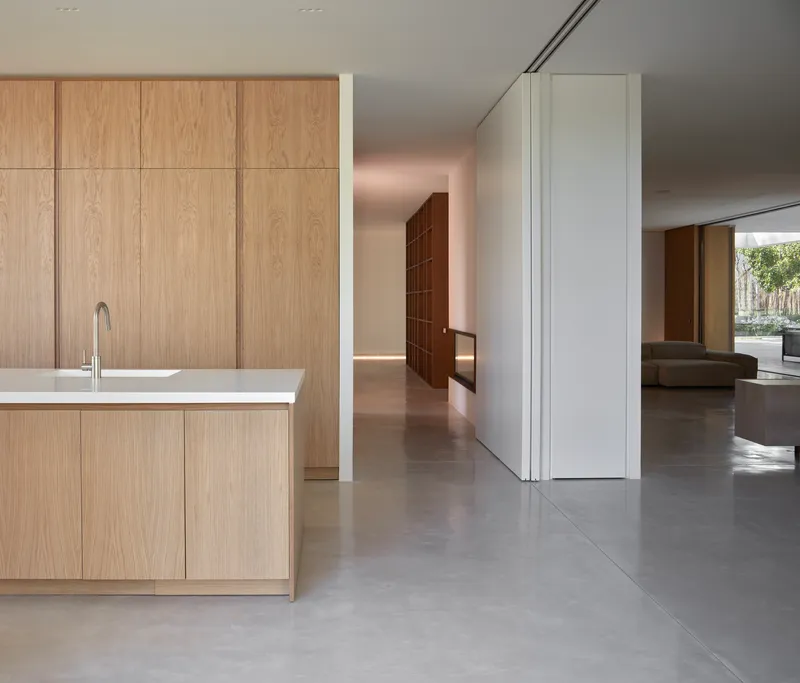Kitchen island with oak cabinetry on polished concrete floor leading to open living spaces