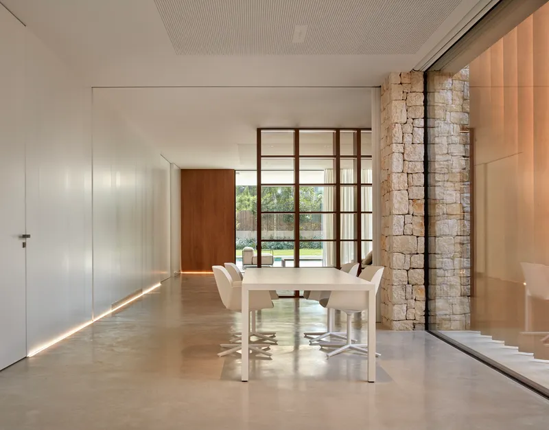 Dining area with glazed wall revealing the garden and dry-stacked stone column beside the table